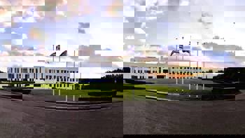A white building with a garden and flags, one of which is the Greek flag